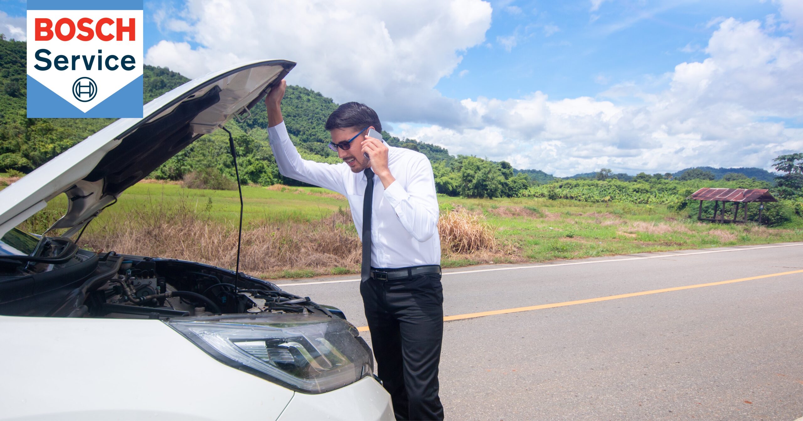 Businessman broken down on side of road, looking under hood of car